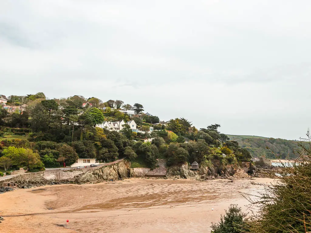 Looking down to the sandy beach with a tree covered hilltop of the other side on the walk from Salcombe to Hope Cove. There are a few houses nestled within the trees.