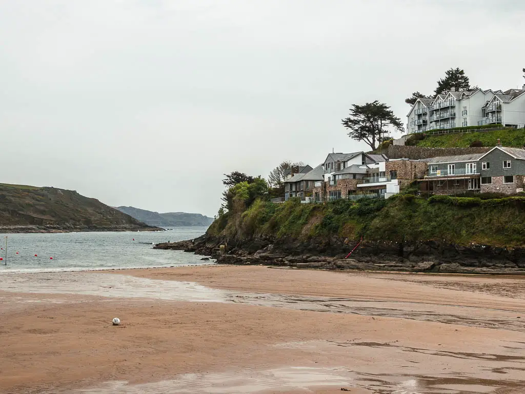 A sandy beach, with a small cliff on the other side. There are houses perched on top of the cliff.