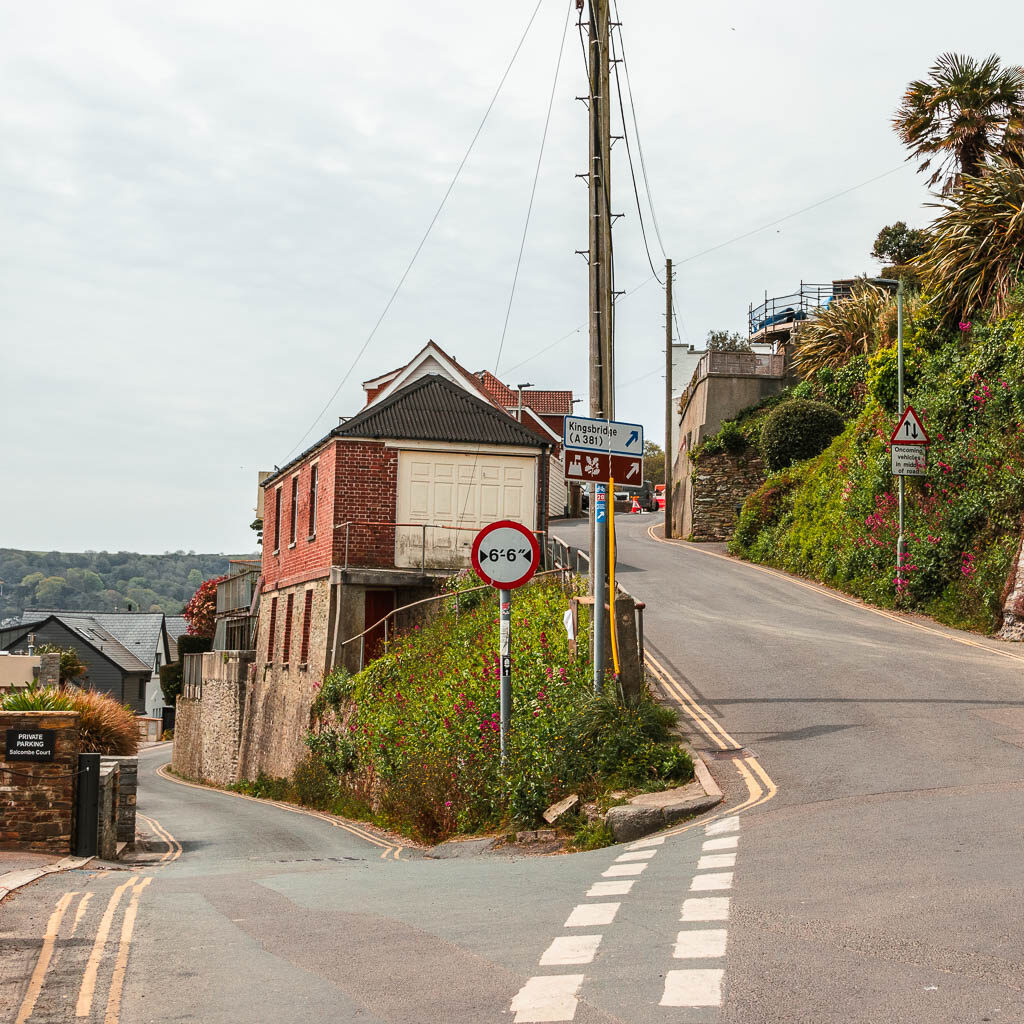 A road spilt with a houses in between. the left road continues level, the right road goes uphill.