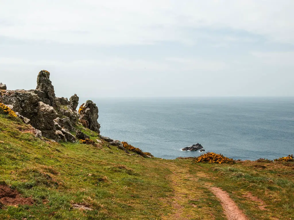 Looking down the grass hill with the blue sea ahead, and some jagged tor outcrops to the left.