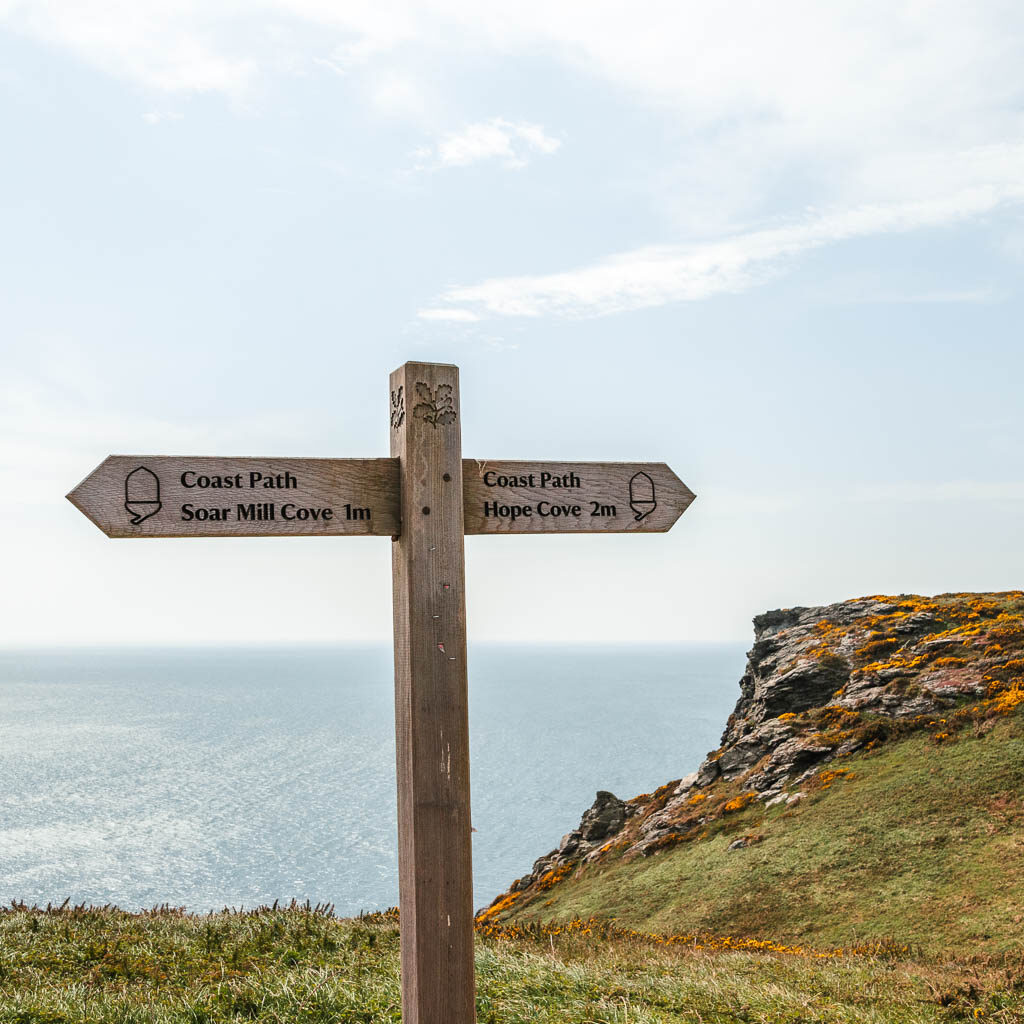 A wooden trail cross sign post pointing right to Hope Cove and Left to Soar Mill Cove.
