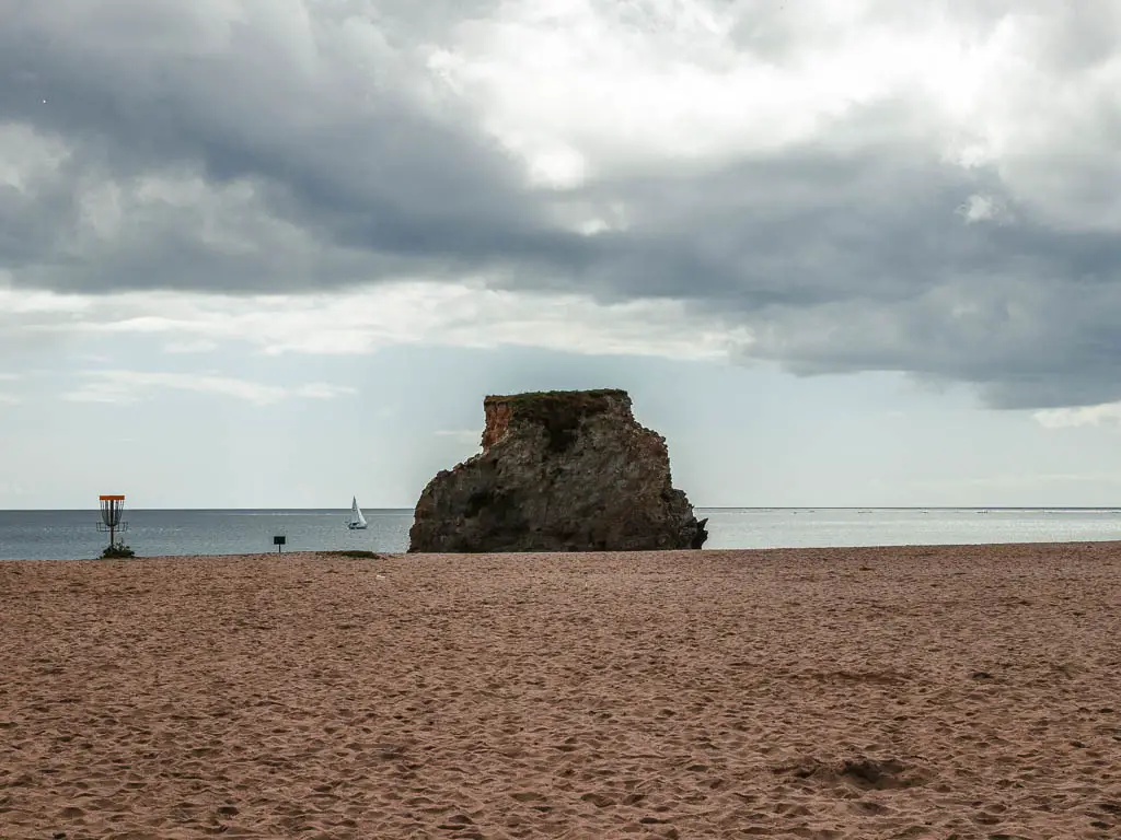 A sandy beach with a large rock straight ahead with the sea beyond that.