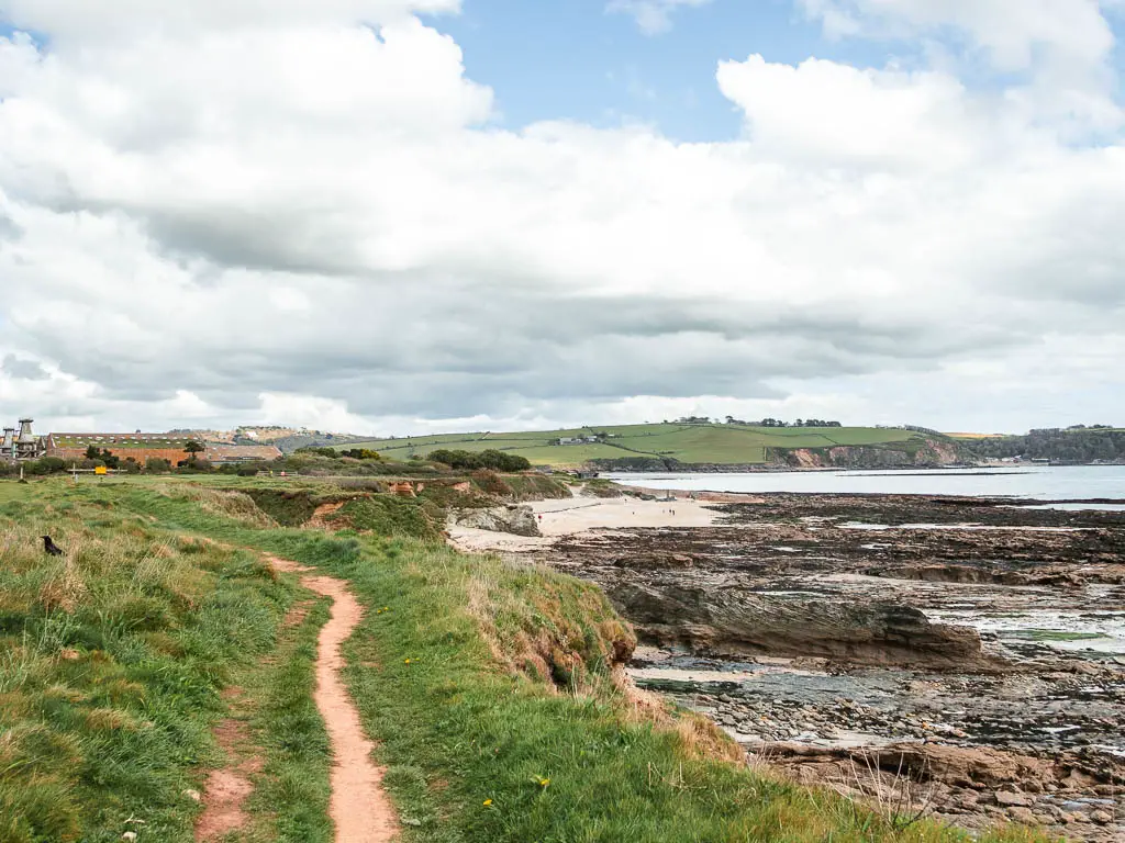 A trail along the grass clifftop, with a view down to the sea and beach ahead to the right on the coastal walk from Charlestown to Par.