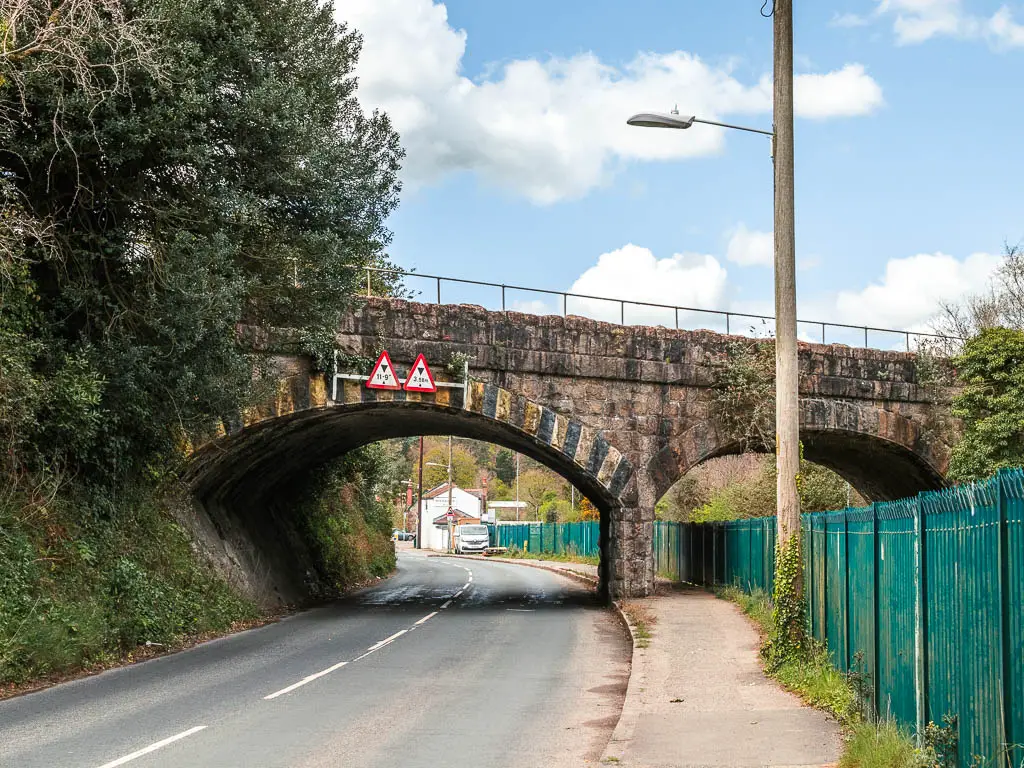 A road as it runs under a large stone bridge.