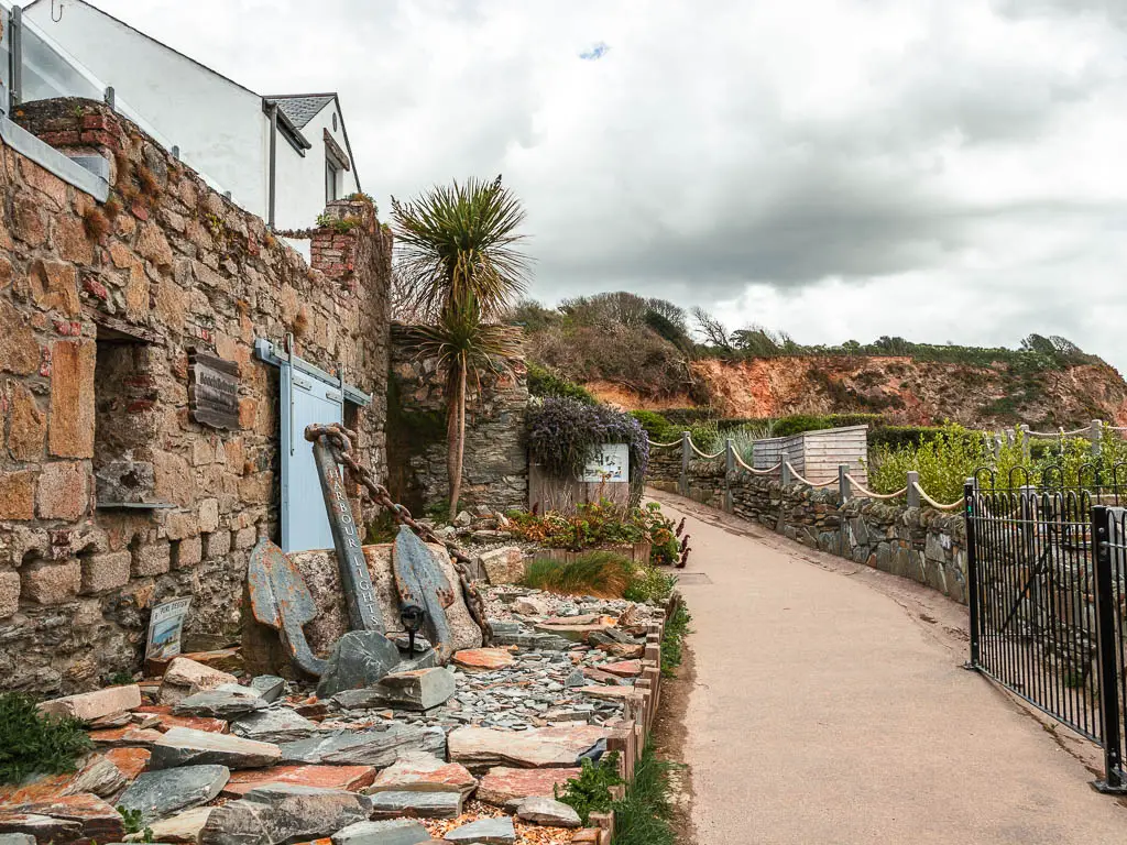 A path on the right and a stone building on the left with a ships anchor displayed outside. 