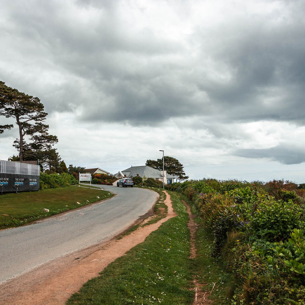 The road as it curves to the left, lined with grass and some bushes on the right.