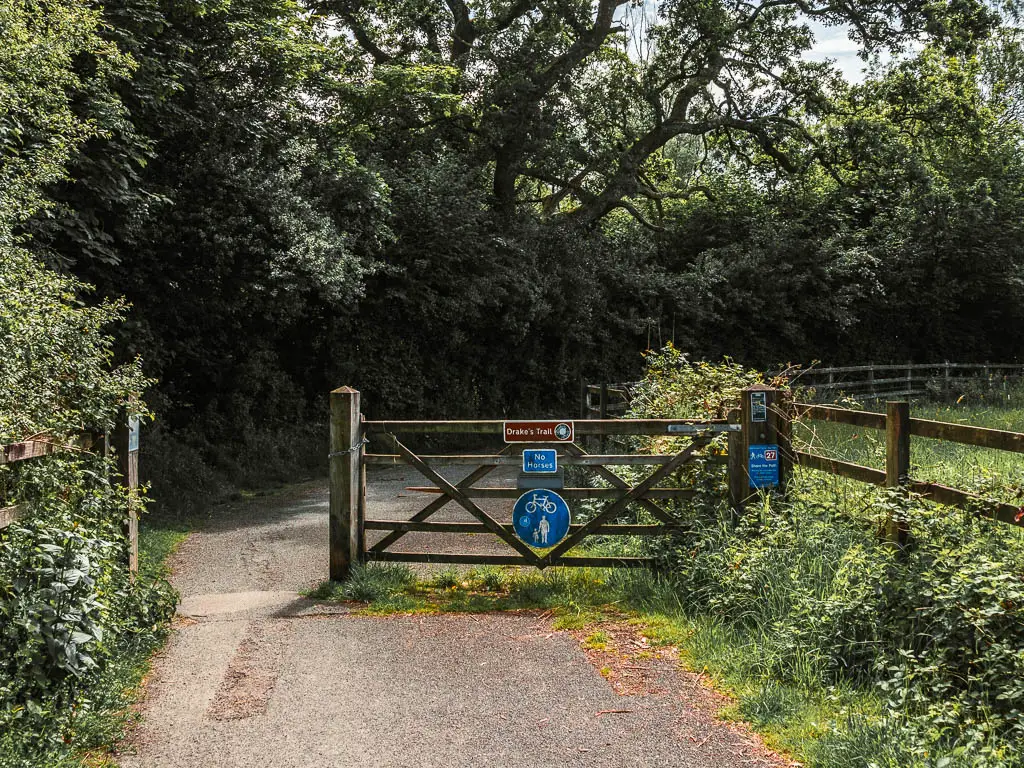 The path leading to a wooden gate with a brown sign that says 'Drakes Trail' and the start of the walk.