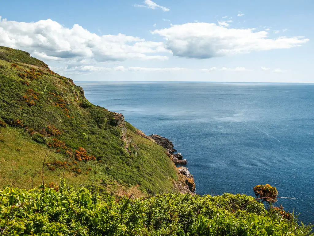 Looking down the side of the grass covered cliff as it meets the blue sea on the right.