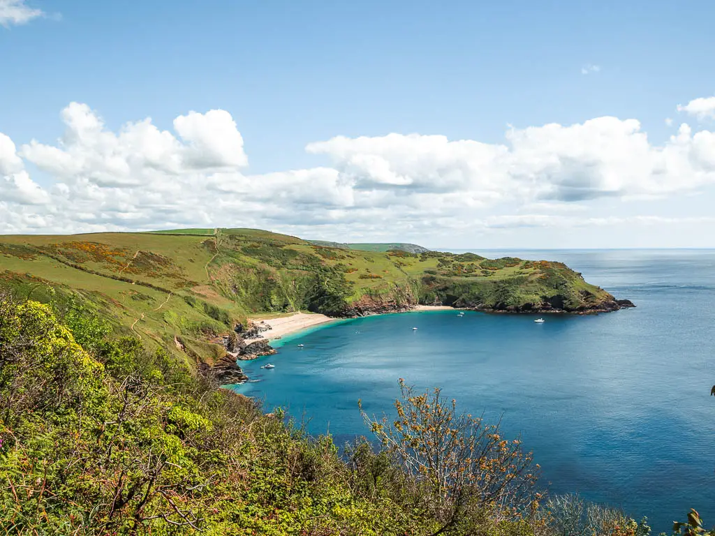 Looking down and along Lantic Bay on the coastal walk from Fowey to Polperro. The bay curves around the left and there a re a couple of white sand beach coves on the other side. The cliff and hill top is covered in grass.