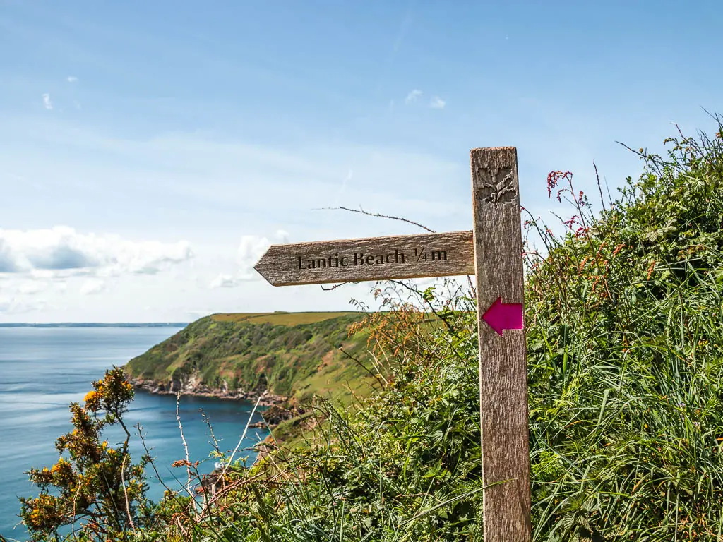 A wooden trail signpost with a pink arrow pointing left to Lantic Bay.