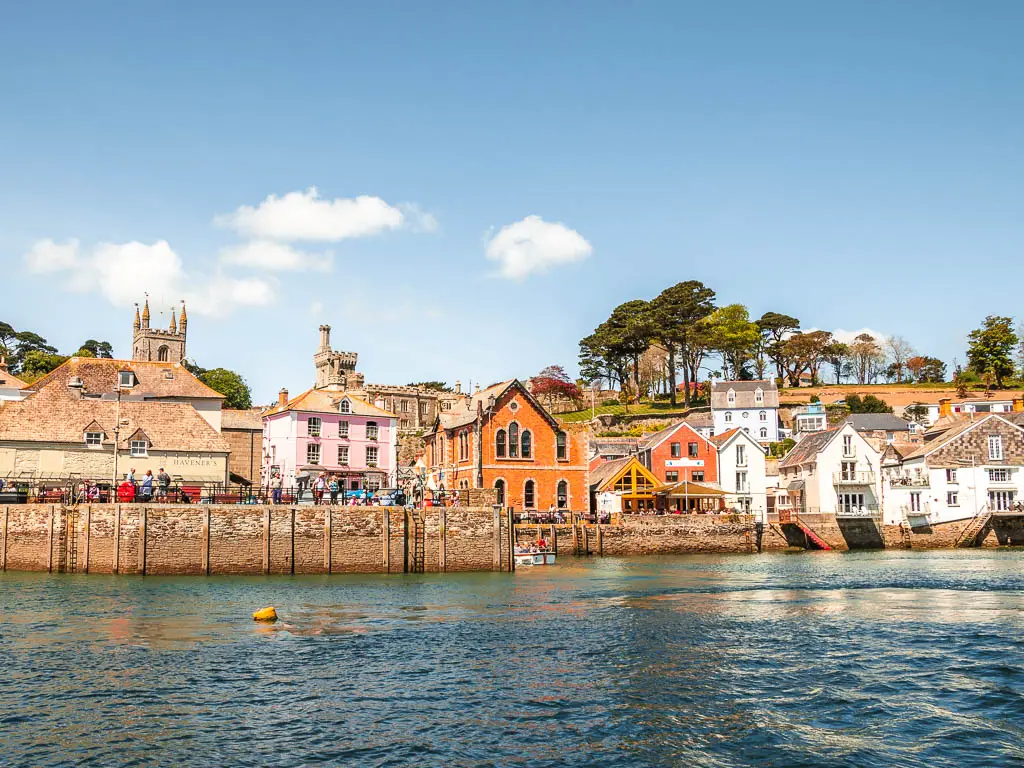 Looking across the water of the Harbour in Fowey at the start of the walk to Polperro. There are orange, pink and white buildings on the other side of the harbour.