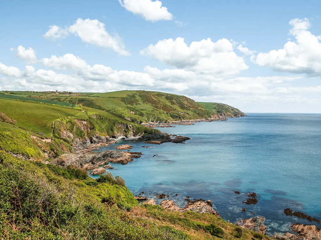 Looking down and along the coastline of Lantivet Bay on the coastal walk from Fowey to Polperro. The coastline is cliffy and rocky, with gras on the cliff and hill tops.