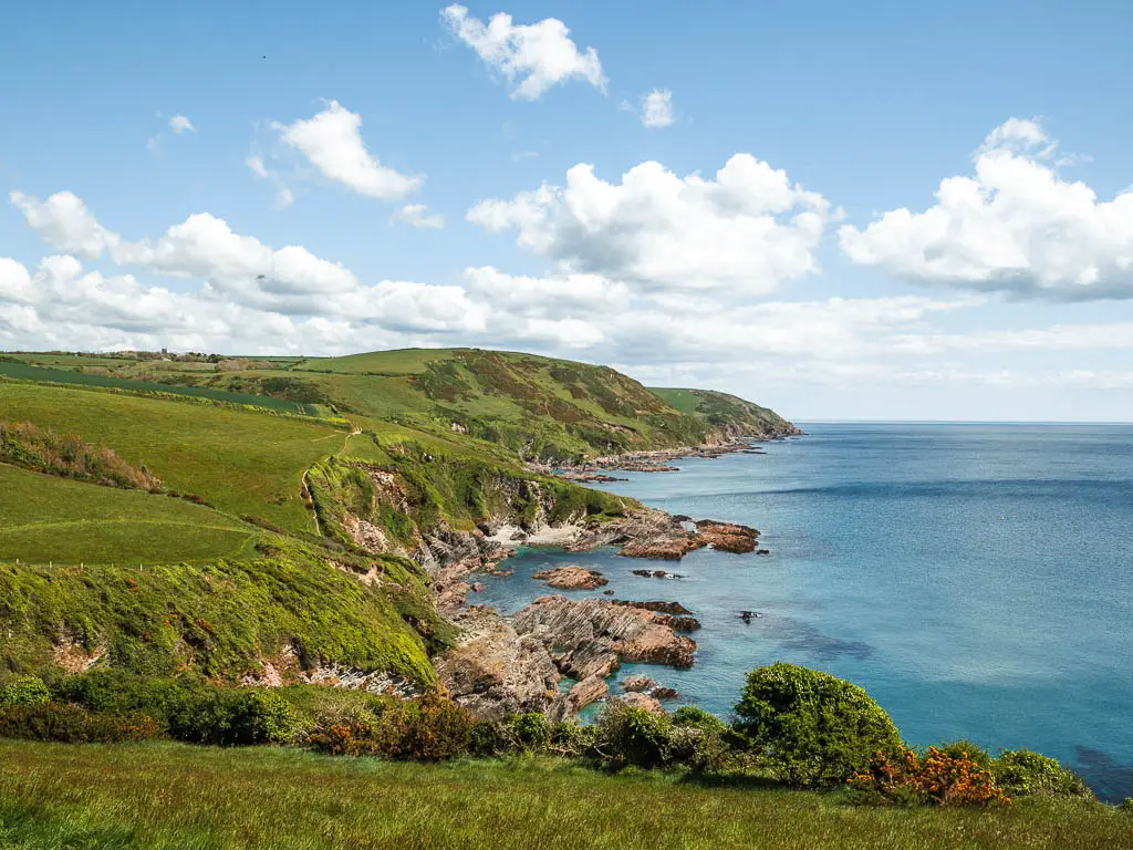 Looking down and along the coastline of Lantivet Bay on the coastal walk from Fowey to Polperro. The coastline is cliffy and rocky, with grass on the cliff and hill tops.