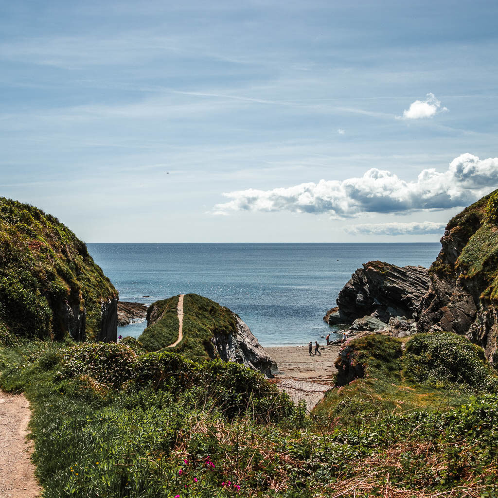 Looking along the top of the grass clifftop to the beach and sea below.