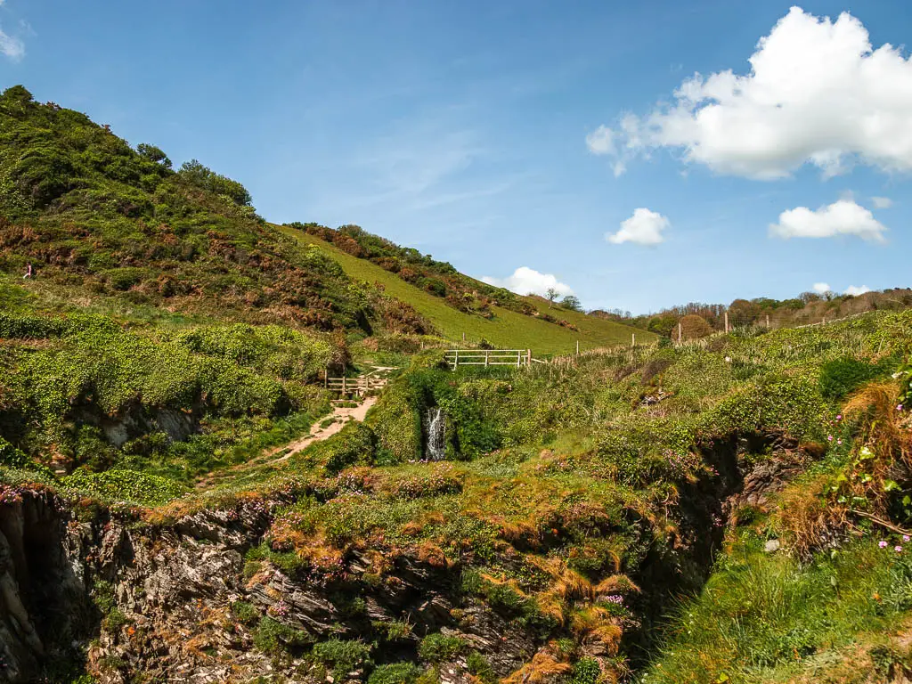 Looking up along the grassy clifftop and then along a valley. There is a small waterfall coming down off part of the cliff.