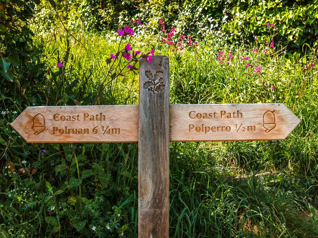 A wooden coast path sign pointing to Polperro on the right and Polruan on the left, near the end of the coastal walk from Fowey.