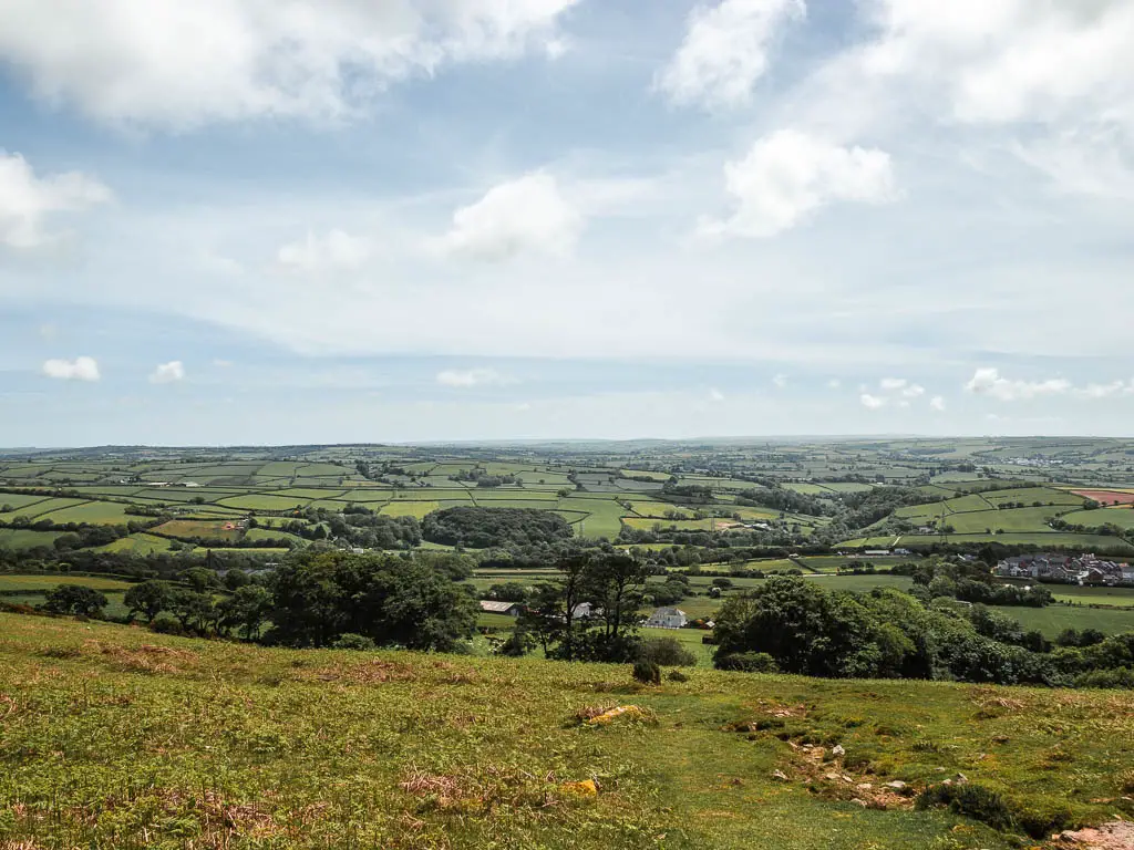 Looking down the grass hill to the green grass field in the distance on the Ivybridge Western Beacon and Redlake tramway walk.