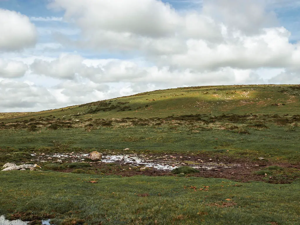 A small path of water at the bottom of a grass covered hill.