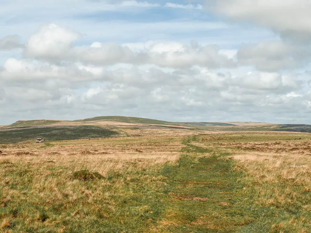 A grass trail running across the moor, with hills visible in the distance.