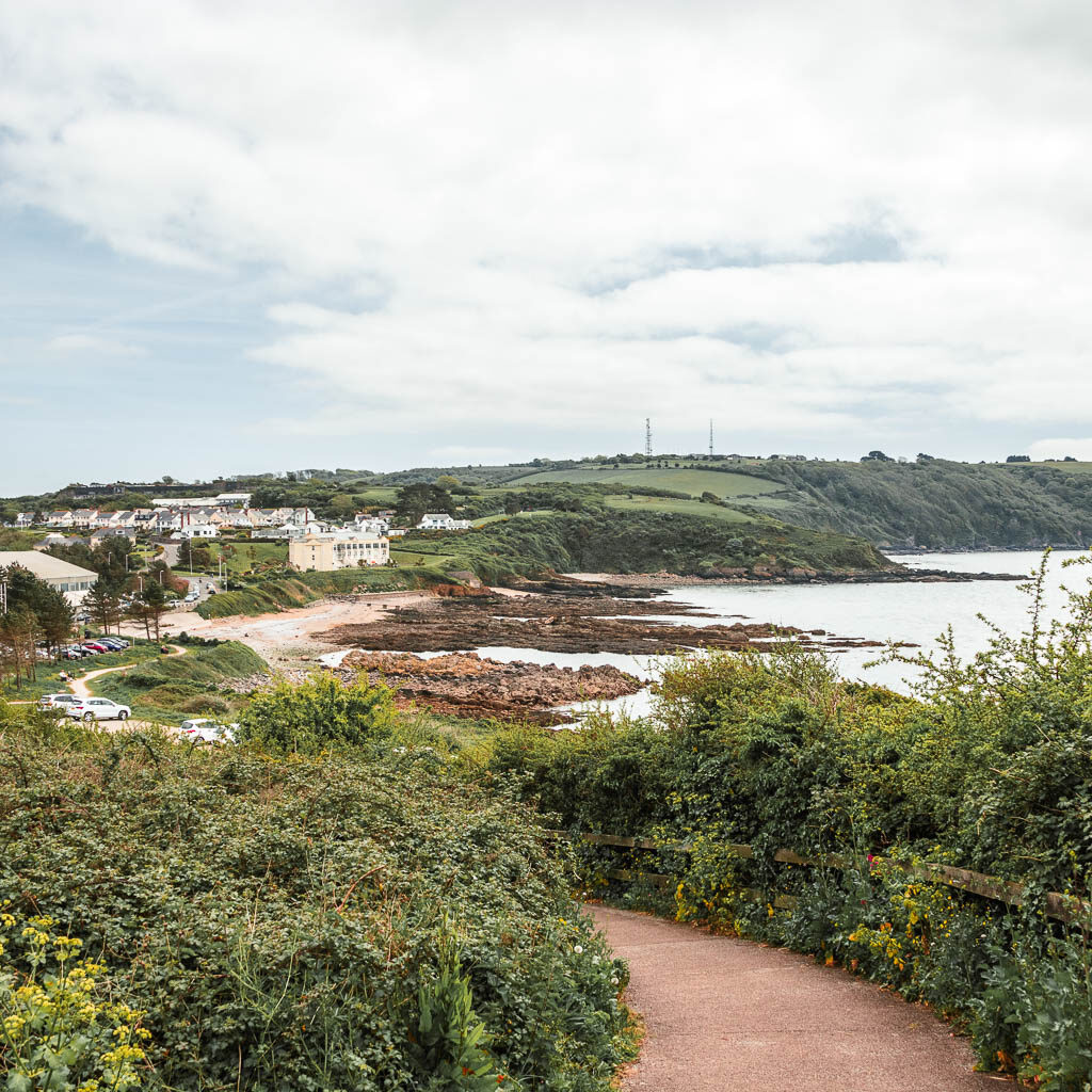 Looking down along the path which is surrounded by bushes, and a view to Jennycliff in the distance. 