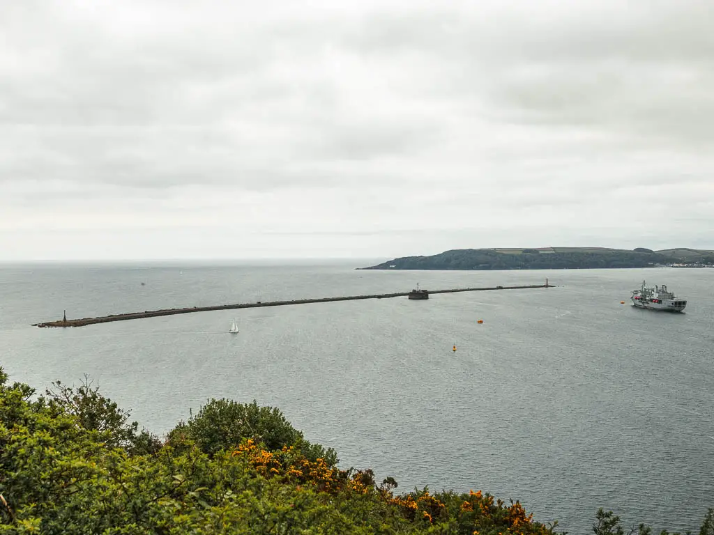 Looking down to the sea and a long thin island. There is a Navy ship to the right.