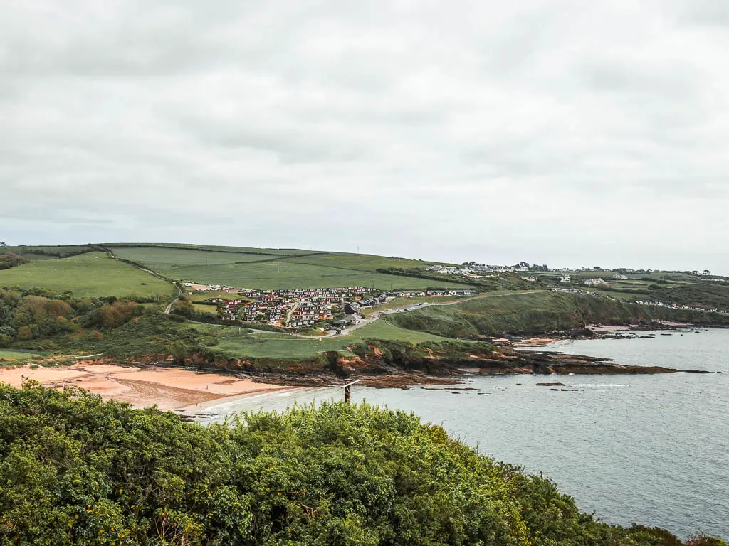 Looking down and over the bushes to Bovisand Beach Cove on the Jennycliff coastal walk. On top of the cliff around the cove is a cluster of houses.