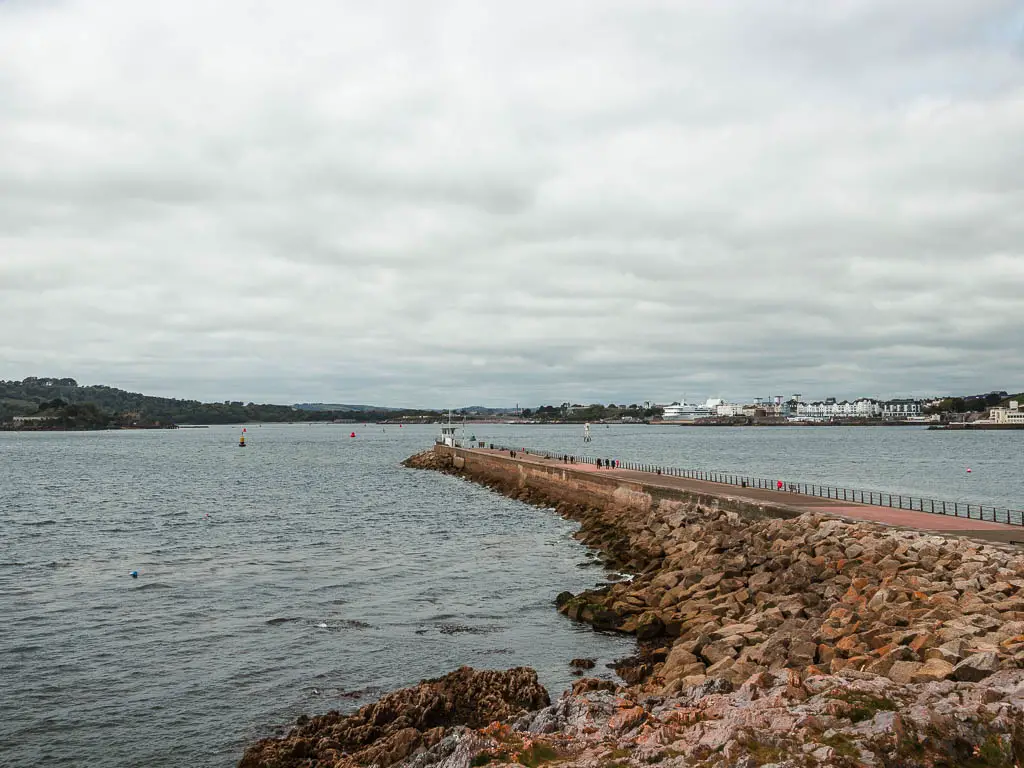 Looking down to the sea and lots of rocks lining the pier, at the start of the coastal walk to Jennycliff.