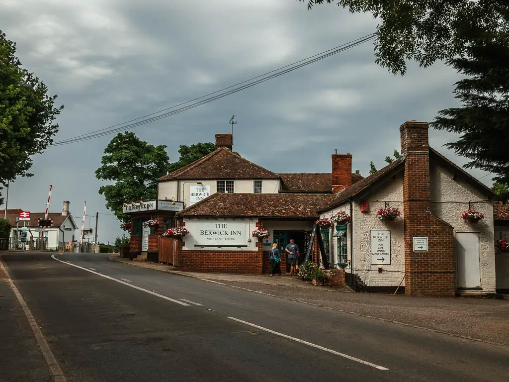 The road, with the Berwick Inn pub to the right, and the railway sign and barrier ahead on the road to the left, at the end of the Long Man of Wilmington walk.