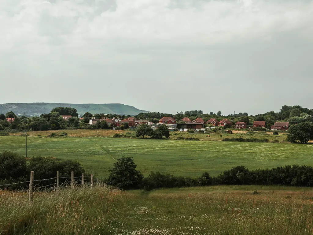 Looking down the hill to a field and village houses in the distance, on the circular walk to the Long Man of Wilmington.