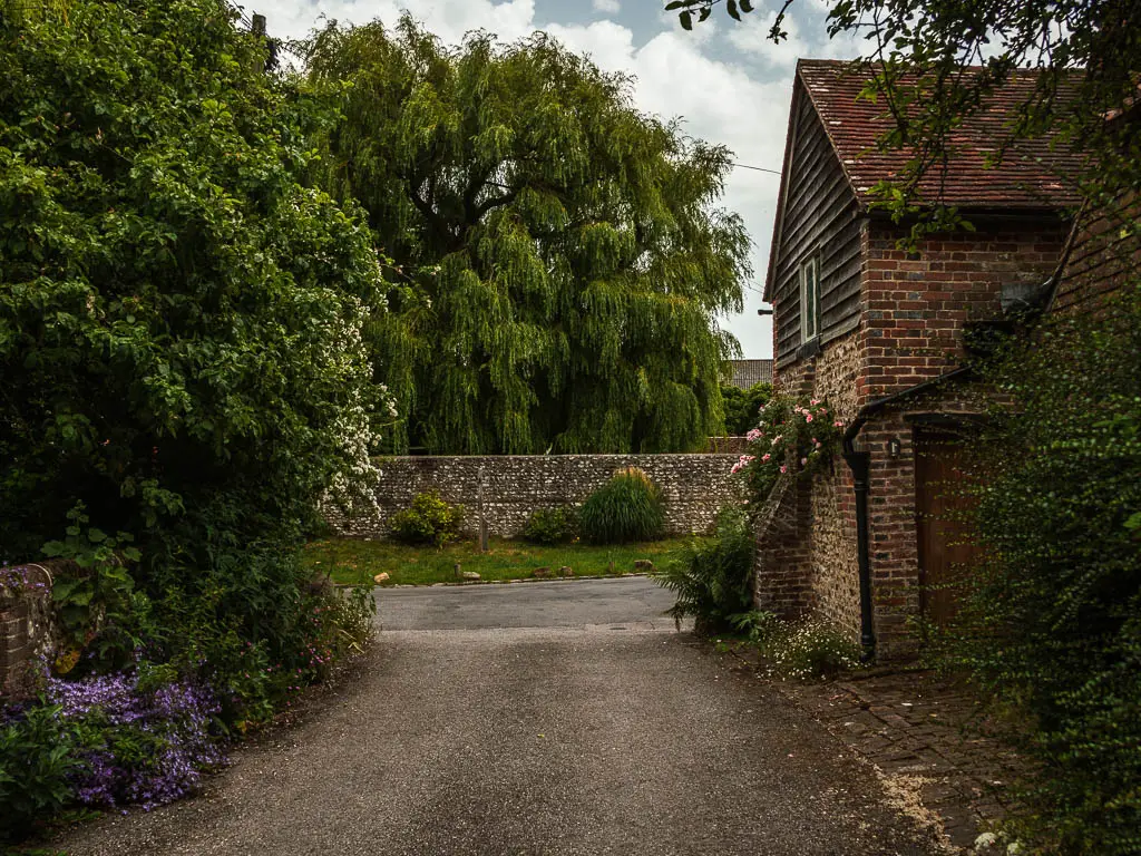 A driveway type road leading to the main road, with a brick house on the right.