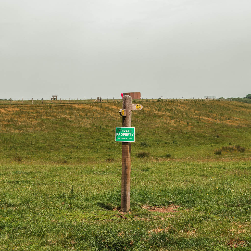 A wooden trail signpost in a green grass field.