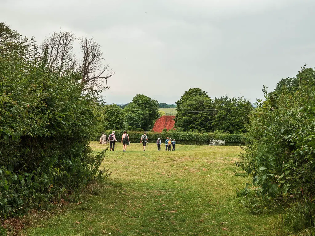 A grass path leading to a big grass field, with people walking in it.