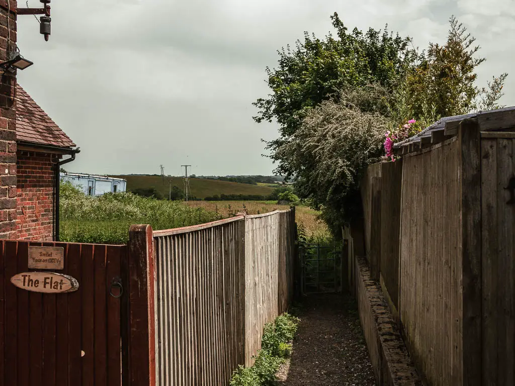 A small path leading between the fences of the hoses, to a field on the other side. 