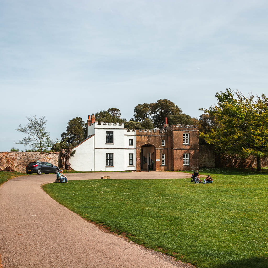 An immaculate path and lawn leading to a large manor building with a white and brown facade. 