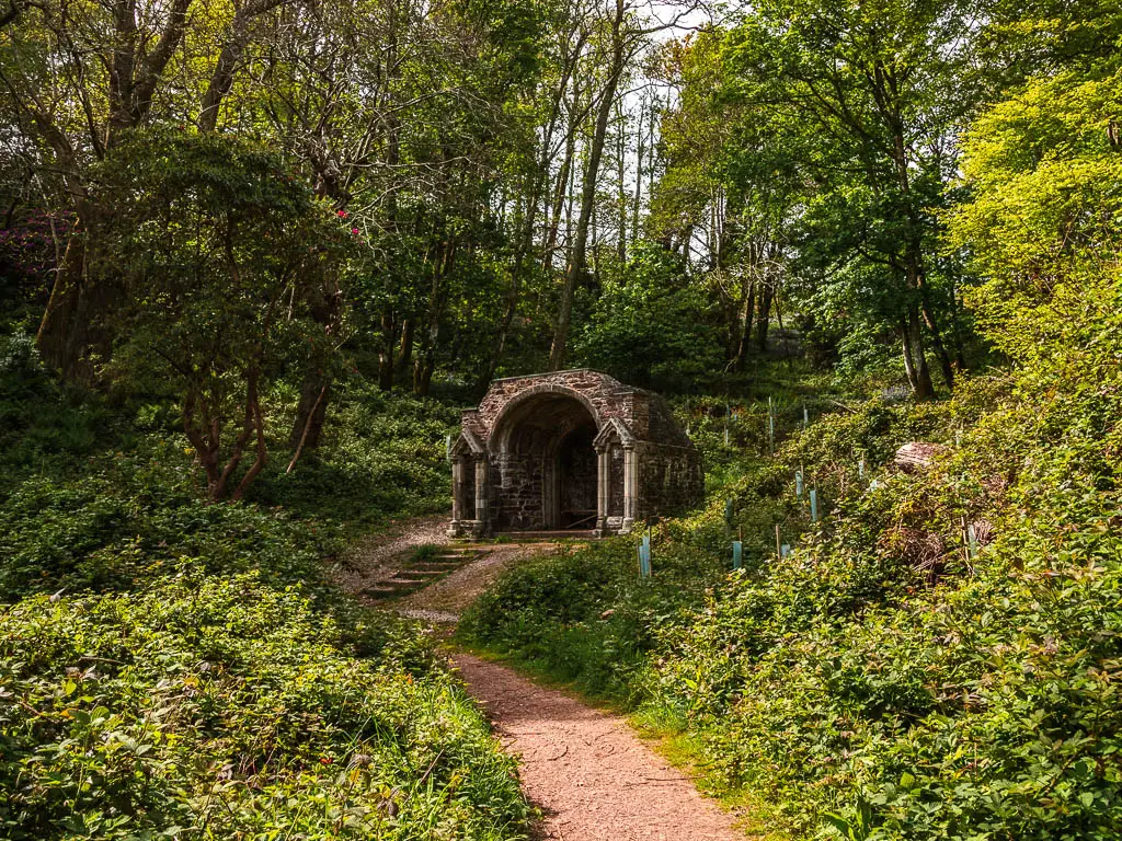 a path leading to the some ruins, surorunded by bushes and trees.