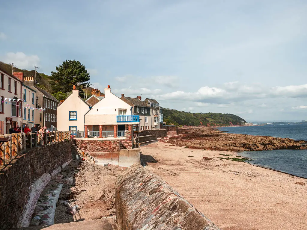 Looking along the sandy beach, with a stone wall and houses left and ahead.