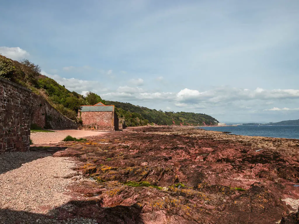 Looking along the rocky coastline towards a stone shed, on the circular walk around Kingsand and Mount Edgcumbe country park.