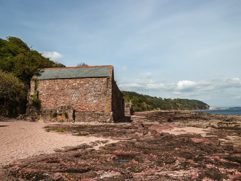 Looking across the rocky and sandy shoreline to an abandoned stone building on the Mount Edgcumbe to Kingsand circular walk.