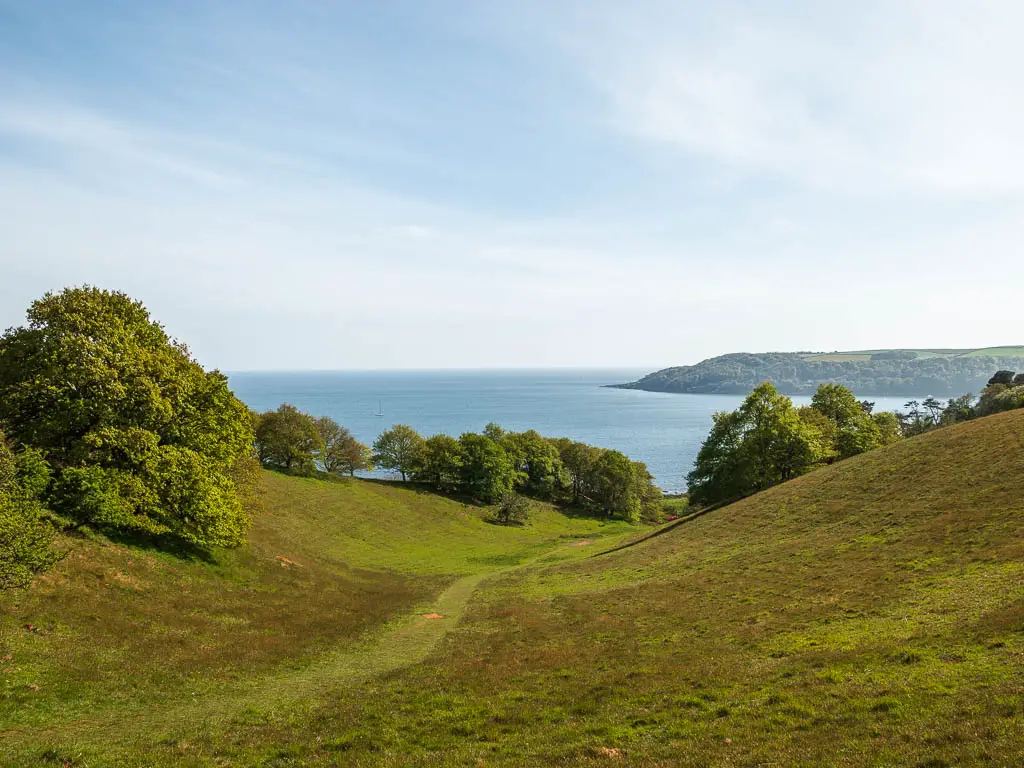 Looking down through the grass hill valley and out to the blue sea on the circular walk from Mount Edgcumbe to Kingsand.