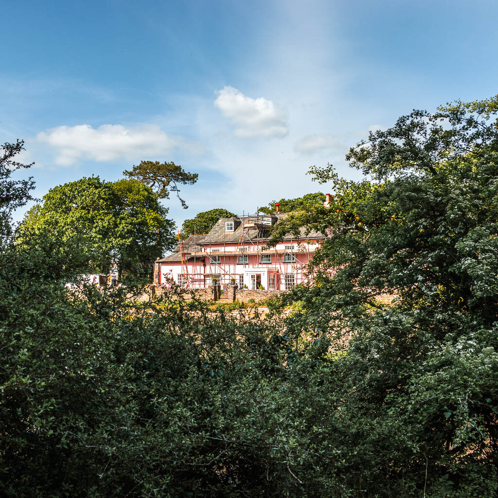 Looking over the bushes to a large house with a pin k facade and covered in scaffolding.