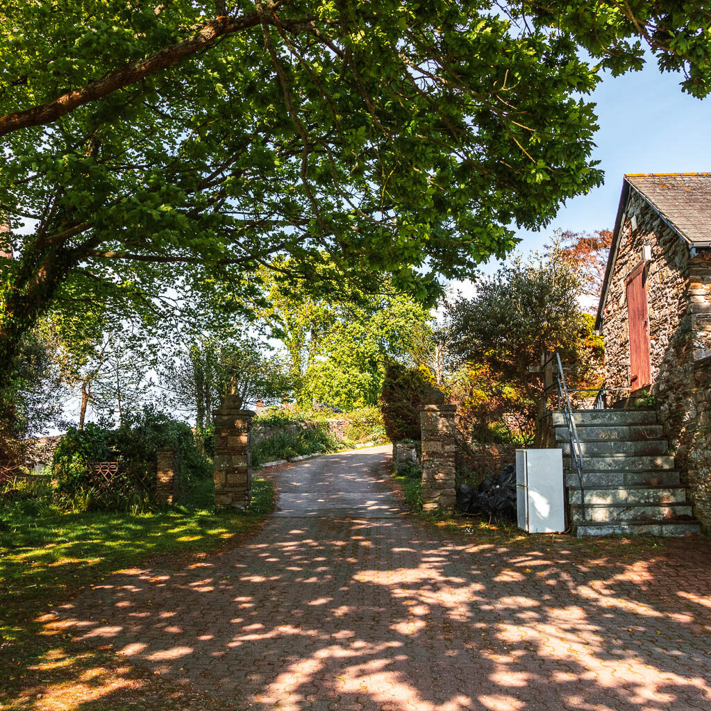 A small road leading up through a stone wall with a stone shed partially visible on the right.