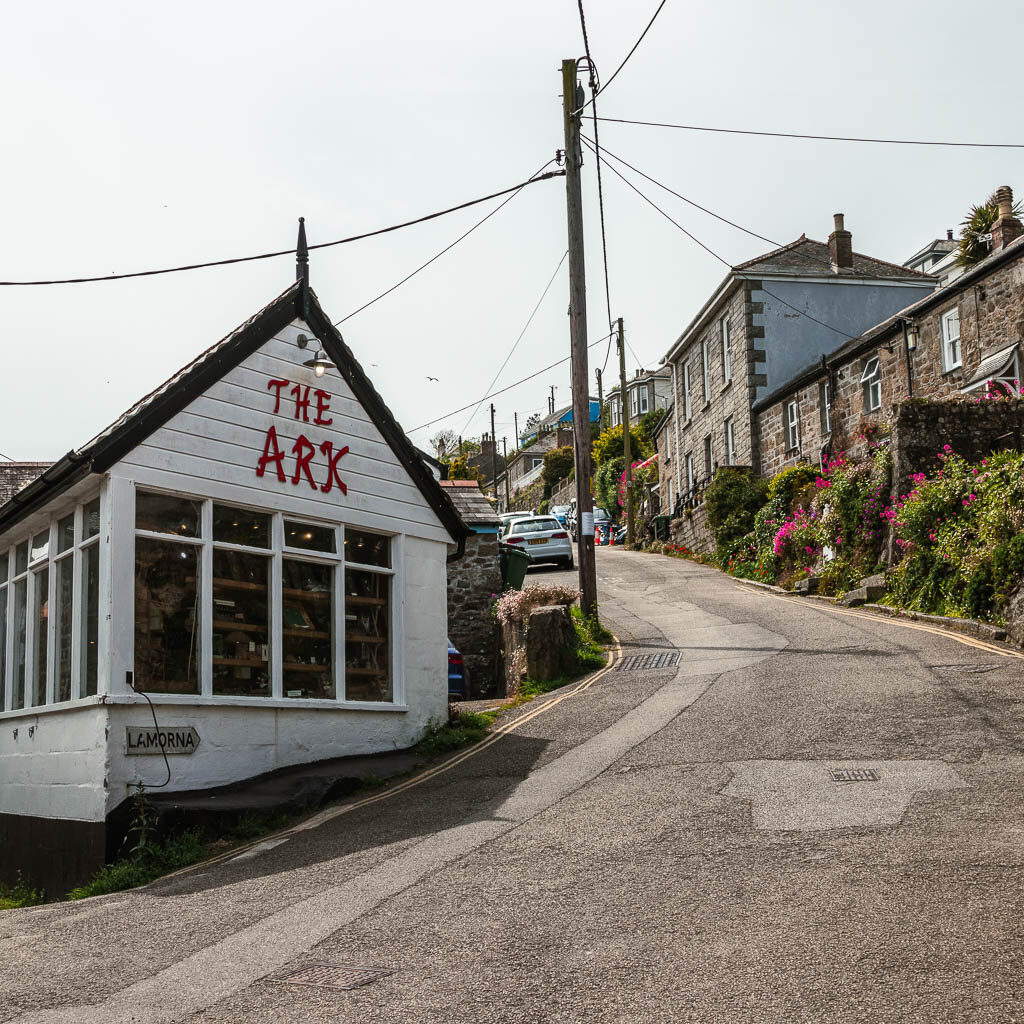 A road leading uphill to the left around a white wood building with 'the ark' written in red. 