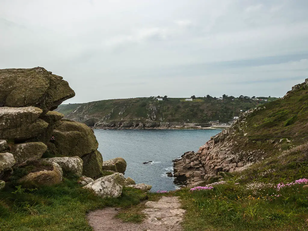 Looking down to the sea on the walk from Mousehole to Lamorna. There are large rocks to the left and a rocky coastline on the right.