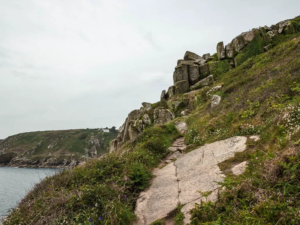 A large slab of rock across the trail on the side of the hill on the coastal walk from Mousehole to Lamorna. There are lots of rocks ahead on the trail.