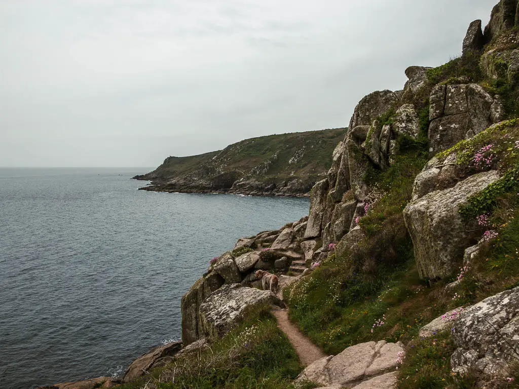 A small trail running across lots of big rocks on the side of the hill on the right with the sea down below on the left, on the walk from Mousehole to Lamorna.