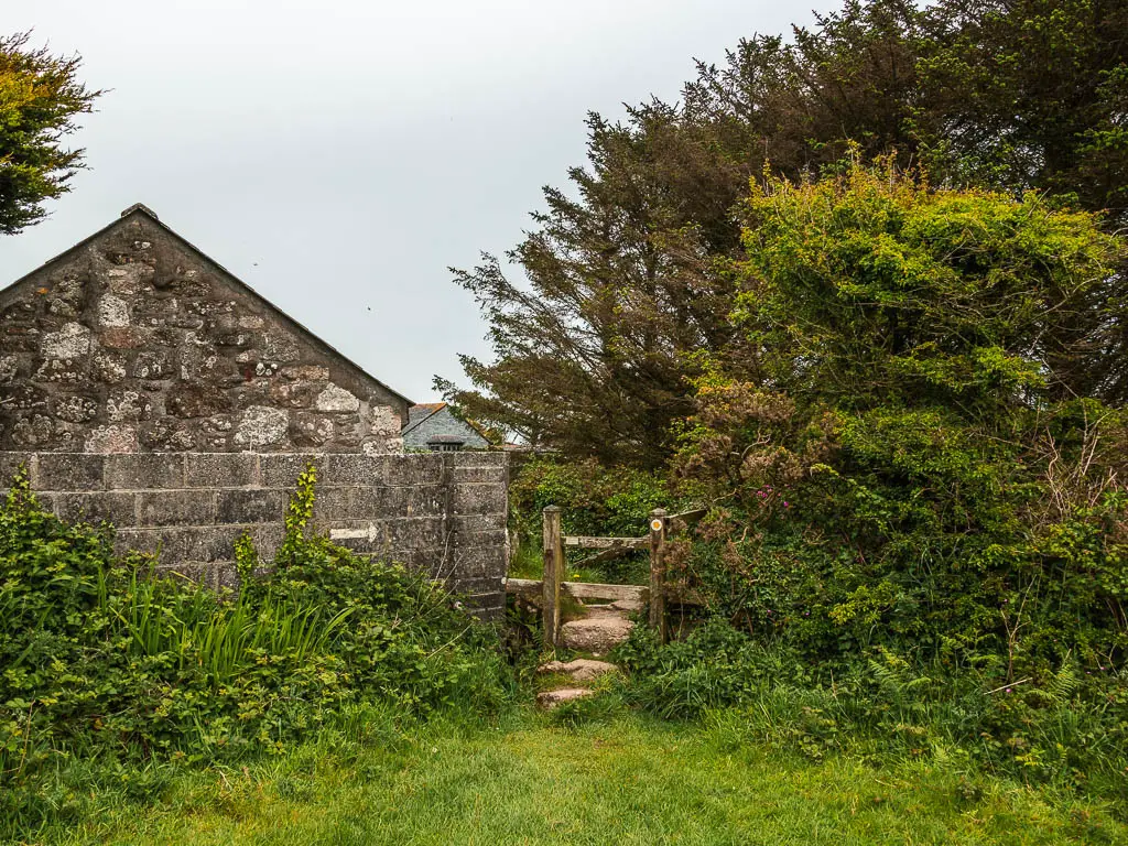 Stone steps with bushes on the right and stone wall on the left. A stone walled house is on the other side of the wall. 