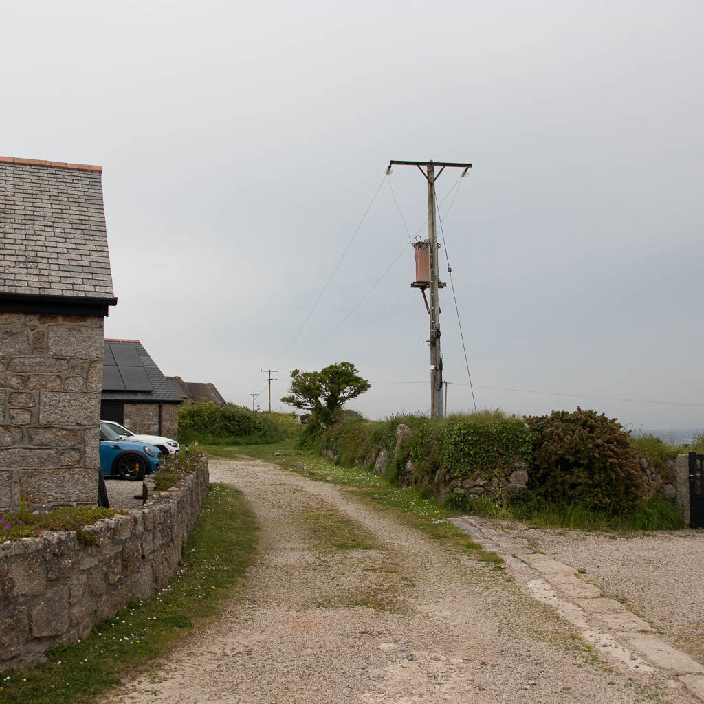 A gravel road, with a small stone wall and houses on the left. 