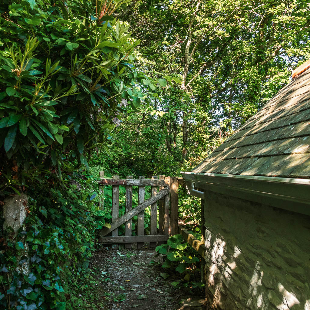 A wooden gate at the end of the cottage, leading into the woods.