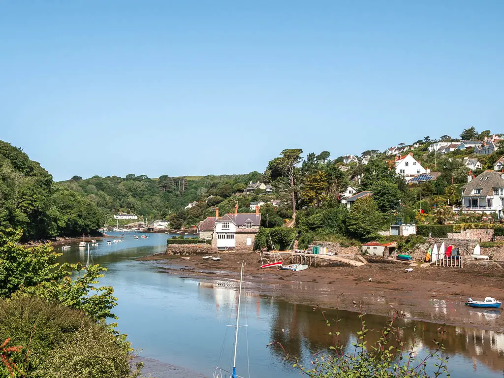 Looking along the river in Noss Mayo at the start of the coastal, circular walk. There are houses nestled with the trees and up the hill on the other side of the river. There are trees lining this side of the river.