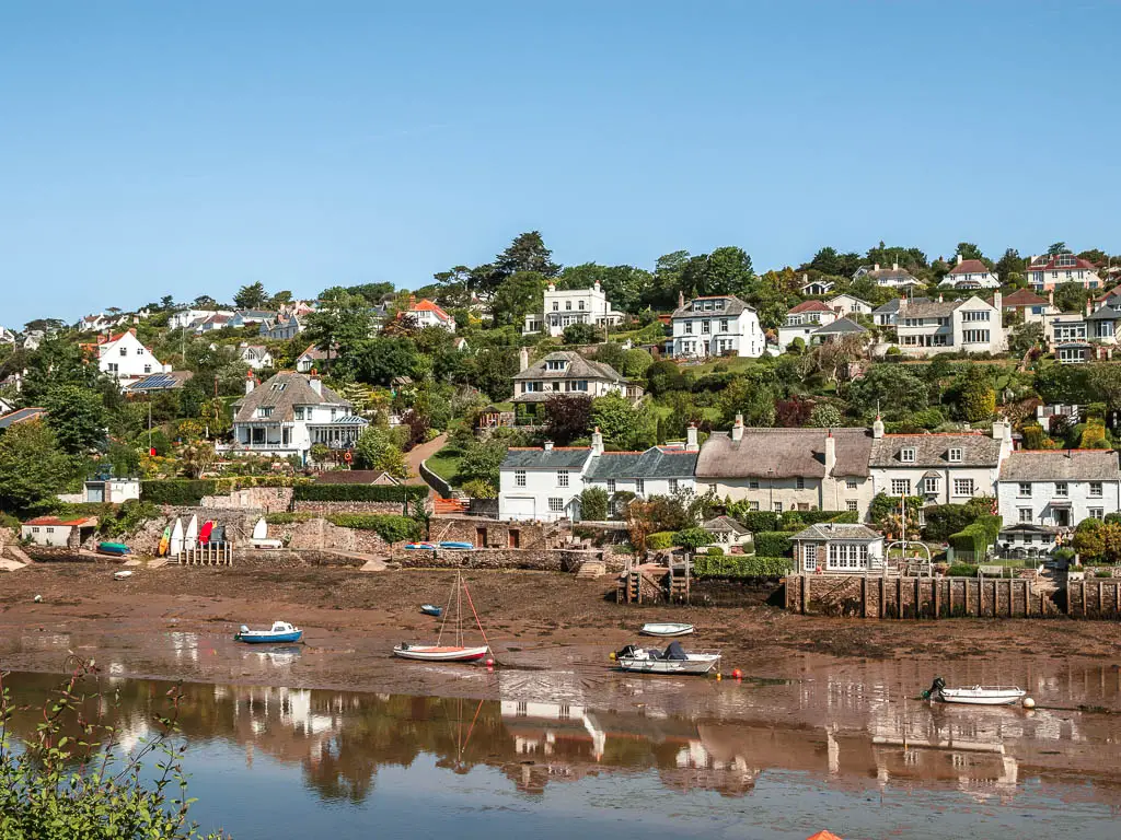 Looking across the river at Lowe tide and village houses up the hill on the other side, at the start of the Noss Mayo circular walk. There are a few small boats resting on the river bed.